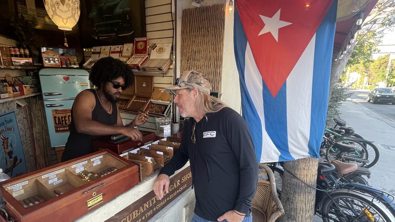 Shopkeeper and customer at the El Cubanito cigar shop counter in Key West, Cuban flag hanging beside them