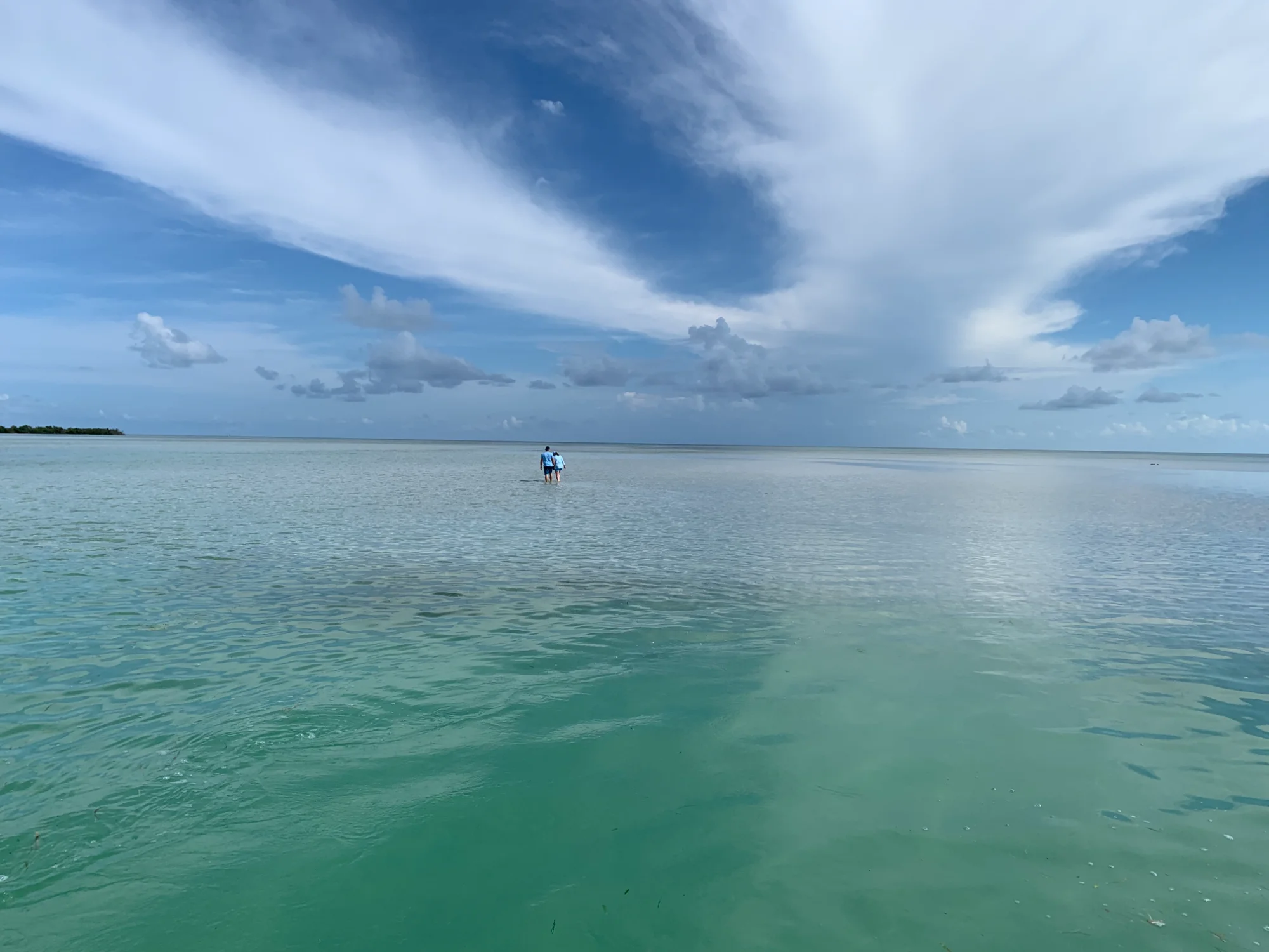 Two people standing far out on a wide shallow sand flat under a big cloudy sky